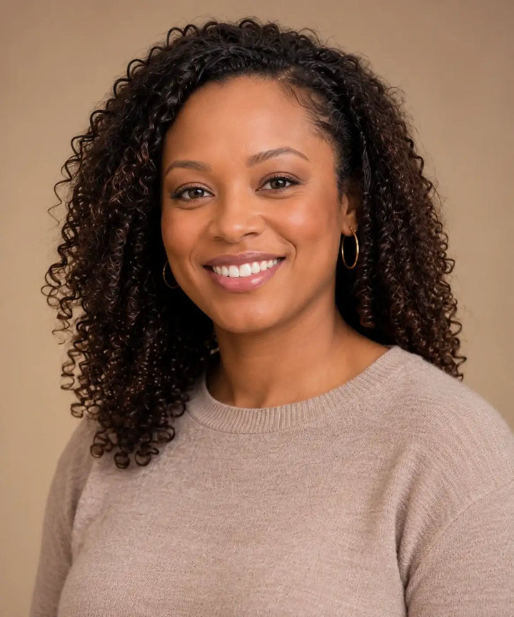 A woman with voluminous dark brown curly hair wearing a soft beige ribbed knit sweater.